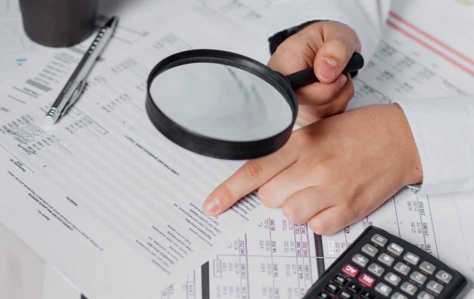 CPA reviewing financial statements with a magnifying glass and calculator